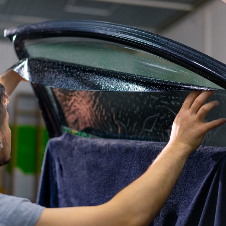 Male car service worker glue window tinting in luxury car detailing car repair